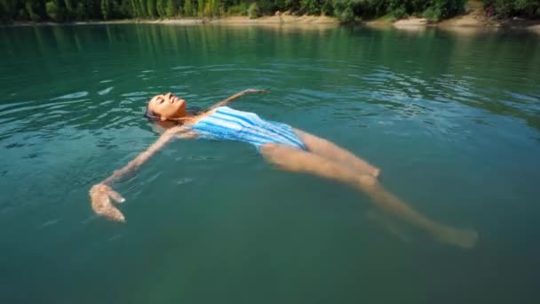 Junge entspannte Frau schwimmt auf dem Rücken im schönen Bergsee mit klarem, blauem Wasser — Stockvideo