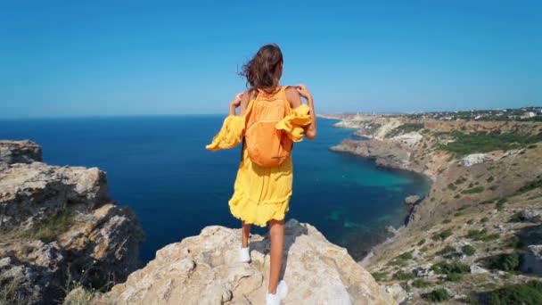 Vista trasera hermosa mujer viajero en vestido de sol naranja de pie en el borde del acantilado — Vídeo de stock