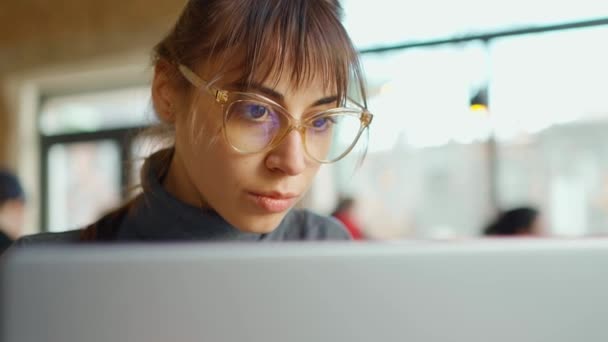 Крупный план лица молодой деловой женщины в очках, сконцентрированной на экране и печатающей на ноутбуке — стоковое видео