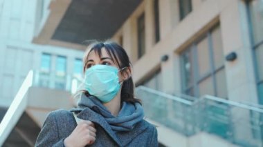 Koronavirüsü korumak için maskeli kadın şehrin aşağısındaki binaların arka planında yürüyor. Konsept koronavirüs salgını, SARS, COVID-19, karantina, izolasyon süresi.