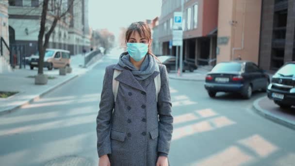 站在空荡荡的城市街道上 戴着防护口罩的漂亮的欧洲姑娘直视着相机 科罗纳韦病毒流行期间空旷的城市街道 — 图库视频影像