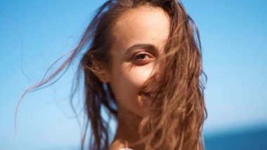 Yavaş çekim güzel bronzlaşmış kadın kumsalda yürüyor ve kameraya gülümsüyor.