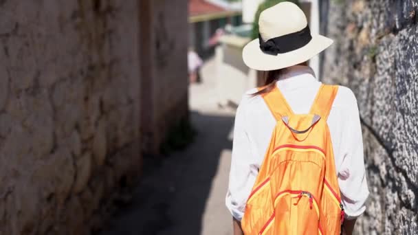 Cámara de visión trasera sigue turista femenina en pantalones vaqueros y camisa blanca caminando en la antigua calle estrecha — Vídeos de Stock