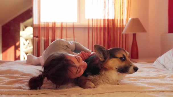Retrato de cerca de la mujer complacida acostada en la cama con su amado perro Welsh Corgi. — Vídeos de Stock