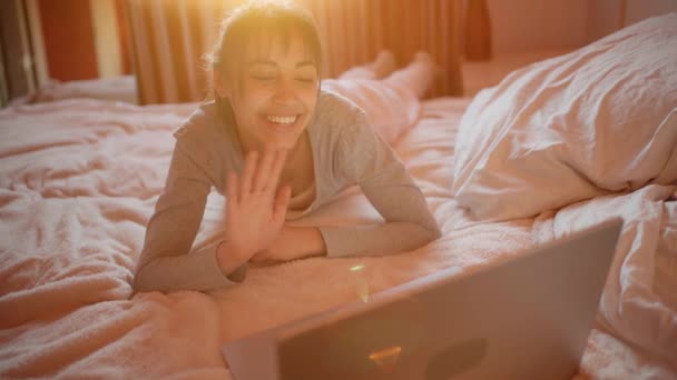 Mujer feliz acostada en la cama en casa y charlando con el novio, teniendo videollamada en el ordenador portátil, utilizando la velocidad inalámbrica de Internet. — Vídeo de stock