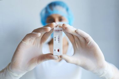 Koruyucu yüz maskesi takan ve eldiven tutan doktor viral hastalık COVID-19, 2019-NCoV için laboratuvar kartı testi yapıyor. Test pozitif sonuç veriyor. Koronavirüs teşhisi, salgın hastalıkların önlenmesi.