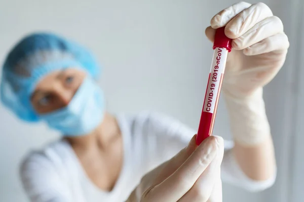 Doctor or laboratory scientist in face mask and glovs holding test tube with blood sample for COVID-19 analyzing. Diagnose checking coronavirus or covid-19 testing result