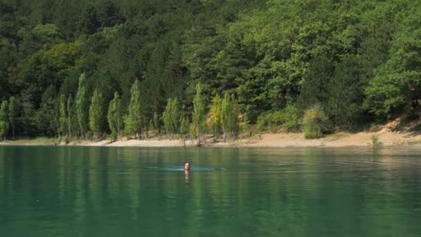 Mladá žena plave v krásné horské jezero s průzračnou modrou vodou na lesním pozadí — Stock video