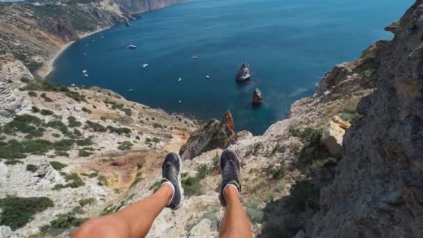 POV első személy megtekintéséhez férfi lábak rövidnadrágban ül a sziklafal szélén csodálatos kilátással — Stock videók
