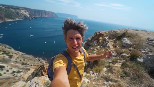 Giovane turista maschio fare selfie e sorridere alla fotocamera sul bordo della scogliera con bella vista sul mare e godersi la natura meravigliosa . — Video Stock