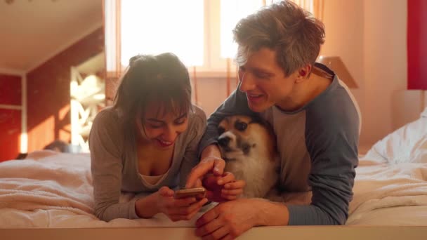 Mooi paar liggend op bed in slaapkamer met schattige Welsh Corgi hond — Stockvideo