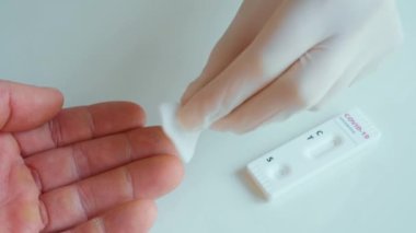 Koruyucu eldiven giyen hemşire hastayı dezenfekte ediyor ve kan örneği almak için parmağını sokuyor.