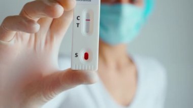Doktor ya da hemşire koruyucu yüz maskesi ve eldiven takıyor. Viral hastalık için laboratuvar kartı testi yapıyorlar. COVID-19