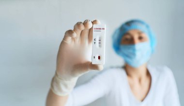 Koruyucu yüz ve eldiven giymiş doktor ya da hemşire ellerinde COVID-19 hızlı test sonucunu tutuyor..