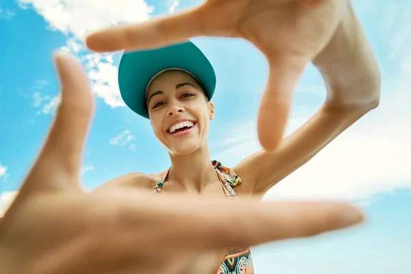 Portrait happy smiling woman making a frame from hands like photo against bright blue sky. Pretty girl in beach cap at sunny day. — Stock Photo, Image