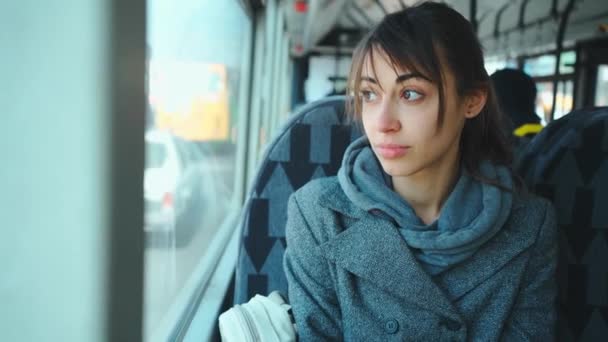 Chica joven en abrigo gris se sienta en el transporte público y mirando a la ventana . — Vídeos de Stock