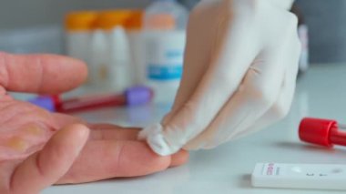 Koruyucu eldiven giyen hemşire hastayı dezenfekte ediyor ve kan örneği almak için parmağını sokuyor.