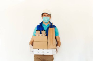 Karantina sırasında teslimat. Koruyucu maskeli kurye ve beyaz arka planda eldivenler paket kâğıt ve yiyecek paketlerini tutuyor.