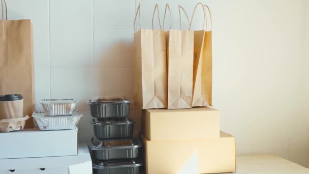 Diferentes recipientes de retirada, pacotes e copos de papelão na mesa contra a parede branca . — Vídeo de Stock