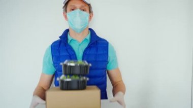 Karantina sırasında teslimat. Koruyucu maskeli kurye ve beyaz arka planda eldivenler paket kâğıt ve yiyecek paketlerini tutuyor.
