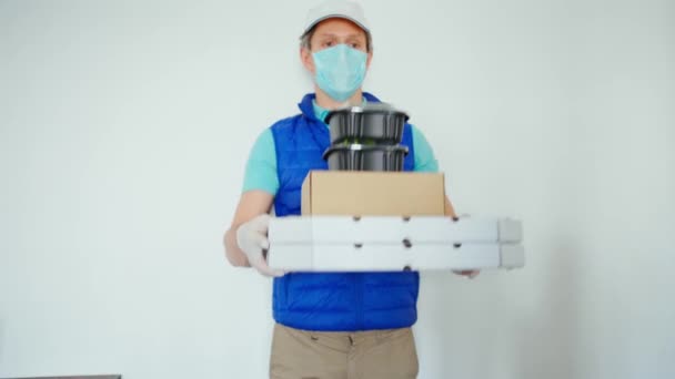 Livraison en quarantaine. Courrier en masque protecteur et gants sur fond blanc contenant des emballages en papier et des contenants pour plats à emporter — Video