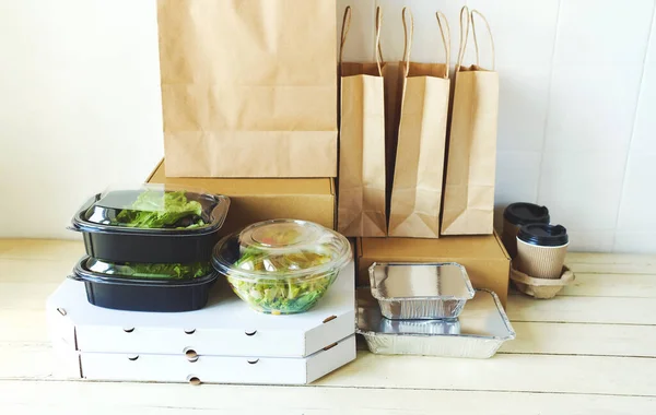 Primer plano paquetes de papel de imagen y contenedores para comida para llevar en la mesa en la habitación blanca brillante . — Foto de Stock