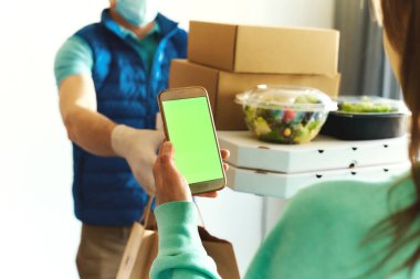 Bir kadının online sipariş vermek için akıllı birini kullanması, teslimatçıdan paket yemek alması....
