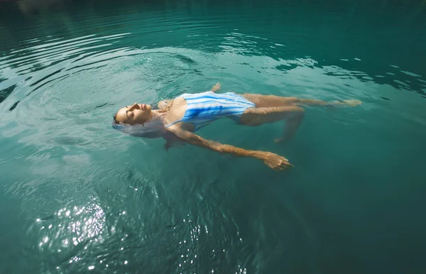 Mujer relajante con los ojos cerrados flotando en aguas tranquilas y claras, nadando en el lago azul . — Foto de Stock