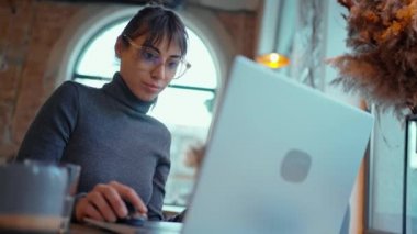 Laptop 'ta, kafede kahve fincanıyla çalışan konsantre bir bayan öğrenci.