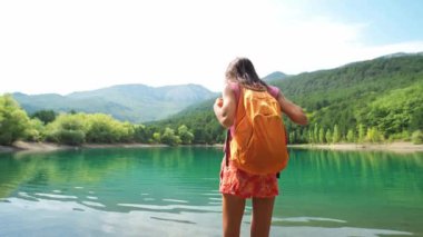 Dikiz manzaralı kadın turist, dağ gölü ve tepelerin arkasında el kaldırıyor..