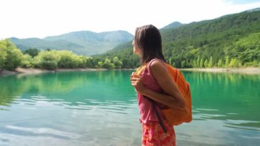 Genç, gülümseyen bir kadın yürüyüşçü güzel dağ gölü manzarasına bakıyor.