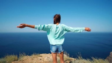 Dağın tepesinde kolları havada bir kadın gezgin.