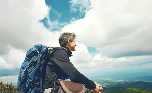 Hombre viajero excursionista con gran mochila relajante y disfrutando de la vista del hermoso cielo nublado en las montañas — Foto de Stock