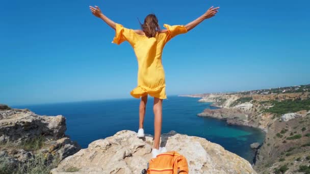 開いた腕で岩の崖の上に立っている日焼けした旅行者の女性の壮大な遅い動き — ストック動画