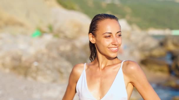 Joven esbelta chica con cuerpo de ajuste perfecto en bikini blanco tomar el sol en el fondo de la costa rocosa — Vídeos de Stock