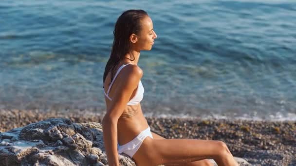 Cuerpo delgado mujer bronceada en bikini blanco relajante en la playa de guijarros — Vídeos de Stock