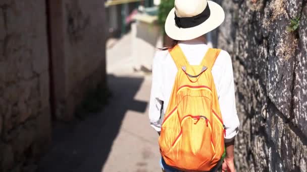 Камера следует женщина турист в белой рубашке и соломенной шляпе ходить по древней узкой улице — стоковое видео