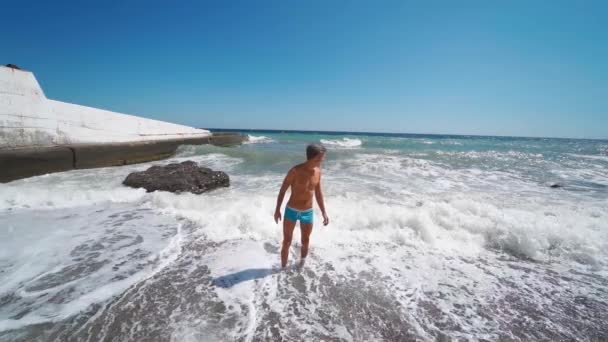 Attraktiver lachender braun gebrannter Mann am Strand mit wehendem Meer. — Stockvideo