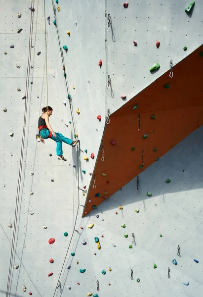 Atletische vrouw klimmer in helder blauw broek swinging op overhangende artificia rots muur met touw. — Stockfoto