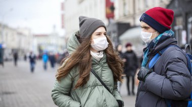  Genç Kız ve Genç Adam Yüzünde Koruyucu Maskelerle Şehir Caddesinde. Konsept - Virüs enfeksiyonunu önlemek. Avrupa. Sıradan. Kapatın. Seçici Odaklanma.