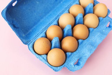 Mavi bir karton kutuda, kahverengi tavuk yumurtaları. Pembe arka plan seti 10 'a izole edilmiş. Sabah kahvaltısında taze yumurta. Sağlıklı beslenme ve sağlıklı beslenme..