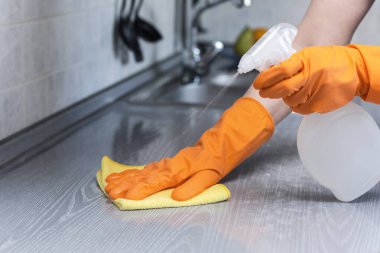 Turuncu koruyucu eldivenli bir kadın mutfak atölyesini sprey ve sarı bir bezle ovuyor. Temizlik konsepti. Yakın plan.