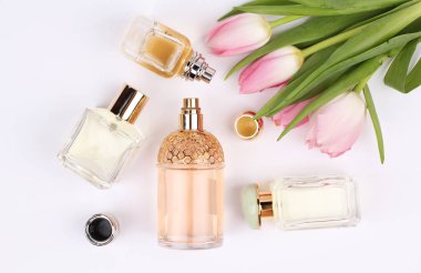 Beyaz arka planda çiçeklerle çevrili parfüm şişeleri 