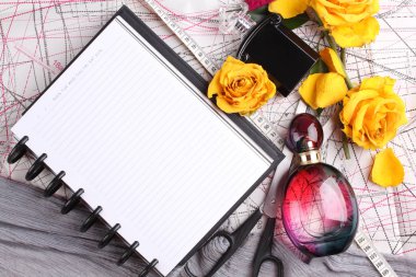 Women workplace top view, flowers, perfume, scissors, blueprints and notebook on wooden background 