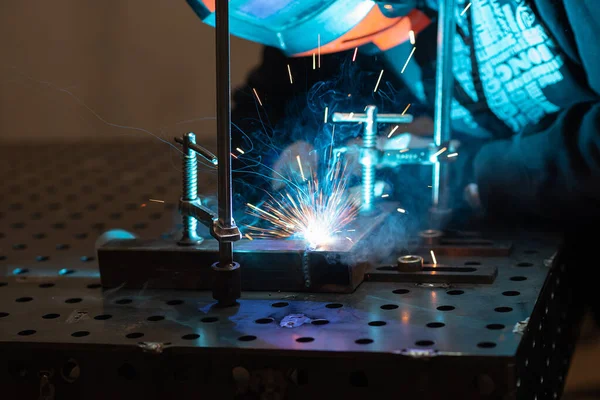 A welder works in a workshop and welds a metal pipe. Welding touches the metal blue sparks and smoke. Concept: work in the workshop, metal welding.