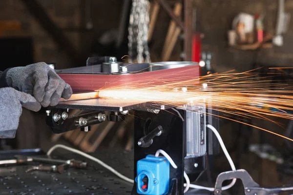 Pracovník průmyslového nářadí brousí hranatou ocelovou trubku na rotačním pásovém brusce — Stock fotografie