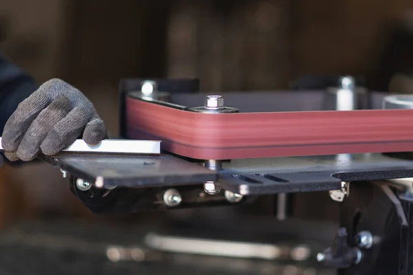 Pracovník průmyslového nářadí brousí hranatou ocelovou trubku na rotačním pásovém brusce — Stock fotografie