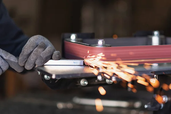 Industrial tool worker grinds a square steel pipe on a rotating belt sander Royalty Free Stock Images