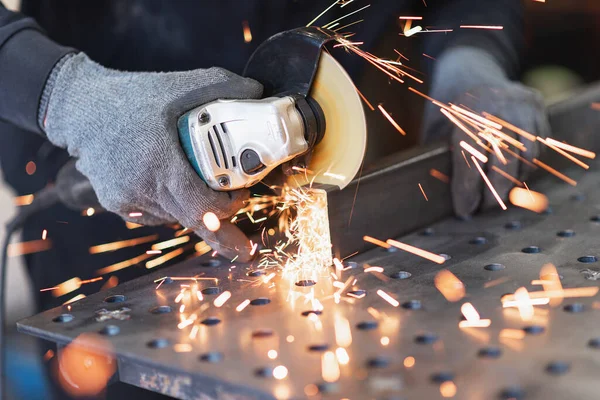 A metal worker cuts a rectangular metal pipe with an angle grinder Royalty Free Stock Images