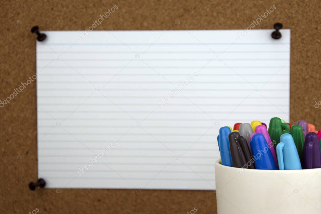 Coloured pens in front of cork board, with flash card in background